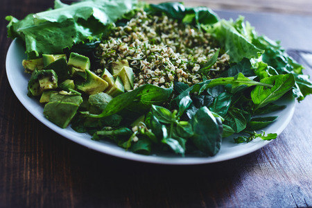 Fresh salad of vegetables and greens on a plate on a wooden background. Salad consists of Sprouted buckwheat grains, Finely chopped dill, zucchini, avocado, lettuce, spinach, Arugula and basil leaves. To the salad served whole-grain bread.の写真素材