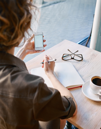 joyful reflective woman sitting in a cafe with notebook at a table made of wood . in the background a bright window with bright daylightの写真素材