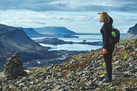 Women travel on a trail in the mountains in Iceland. A woman stands on the edge of the fjord and looks at the landscape towards the fjord and the bayの写真素材