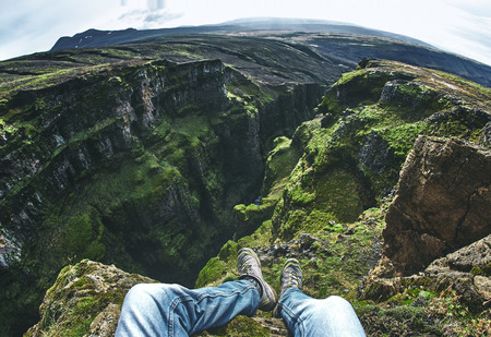 travel and Hiking to Icelands highest waterfall - Glymur. hiker makes selfi by photographing his legs from above. A man is sitting on the edge of a cliffの写真素材