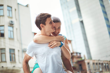Young people, couple having date on the street. A loving couple on a date on a summer evening. The guy with the girl hugs and kisses. Youth, first feelings, first love, first dates. The girl jumps the guy on the backの写真素材