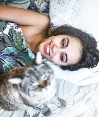 Happy beautiful young woman in the morning in bed with a cat. A woman without clothes and covered with a blanket. Morning photograph with a natural light from the window at home. Good mood and a pleasant start to the dayの写真素材