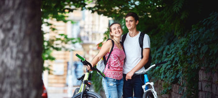 Young people, couple with bicycles in the park. A loving couple on a date on a summer evening. The guy with the girl hugs and kisses. Youth, first feelings, first love, first datesの写真素材