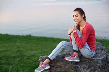 beautiful young girl in a pink jacket sits on the green field and happy smilesの写真素材