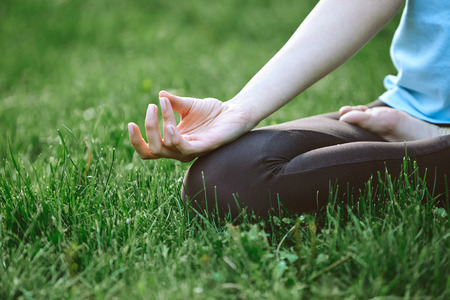 Portrait of young and sporty woman in sportswear doing yoga or Stretching exercises outside at the park on green field on cloudy day, Dnipro, Ukraine. She is sitting on the green meadow between treesの写真素材