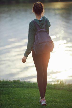 Portrait of beautiful happy girl in sportswear with small urban backpack on the shore of a lake or sea. woman makes selfie photo or video call.の写真素材
