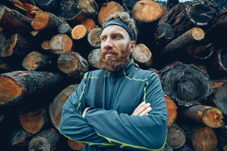 Stylish severe bearded man amid a pile of logs, posing like lumberjackの写真素材