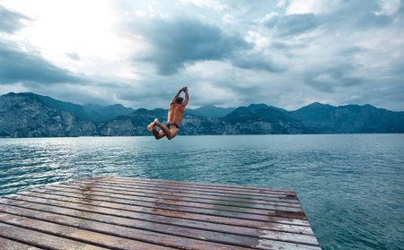 man jumping into the water from the pier. Lago di Garda lake, Italyの写真素材