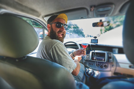 funny smiling bearded man with glass of wine in the car on the driver place