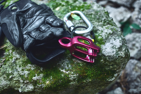 climbing equipment on the old stone with moss. climbing belaying device and carabine and black leather glovesの写真素材