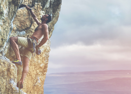 adult man rock climber. rock climber climbs on a rocky wall. man makes hard moveの写真素材