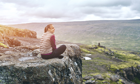 Girl in warm clothing sits on the cliff on background of mountains of Iceland.の写真素材