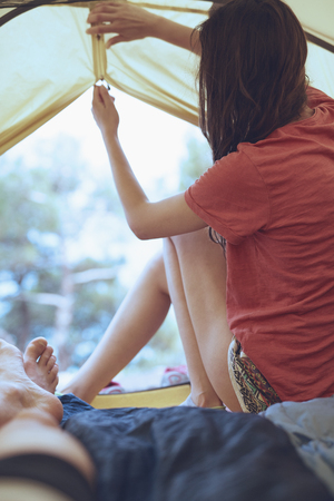 view from inside a tent at the forest and woman emerge from tent. travel and hiking concept, Tourist tent inside with peopleの写真素材