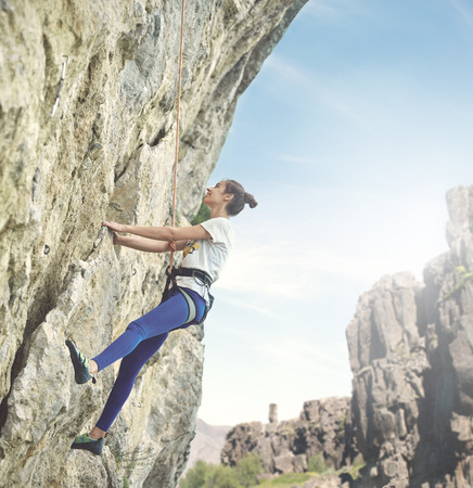 young cheerful woman climbs on the cliff. rock climber Learns to climb rocks on a rocky wall. woman makes hard move and looking upの写真素材