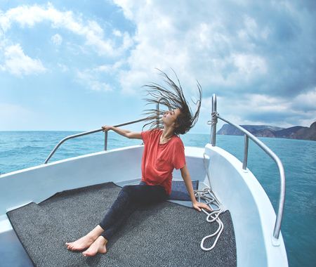 happy young smiling woman in the white boat on the cloudy sky background. woman wearing in a red t-shirt looks very happy. Caucasian female modelの写真素材