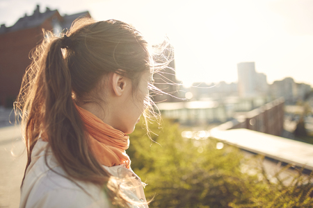 back view of a beautiful young woman in a beige cloak and in an orange scarf on the city walk in autumn.の写真素材