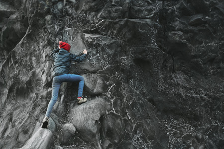 woman rock climber. rock climber climbs on a black rocky wall on the ocean bank in Iceland, Kirkjufjara beach. woman makes hard move without rope.の写真素材