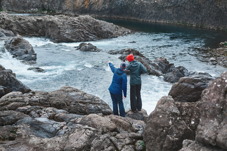 a women tourists in waterproof clothes stands on the Bank of the mountain river with small waterfall. Glanni waterfall, Icelandの写真素材