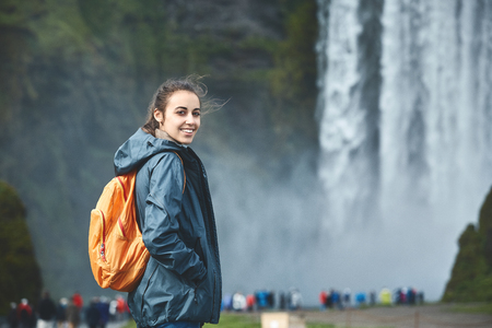 Girl in waterproof clothing stands on background of Skogafoss waterfall in Iceland.の写真素材