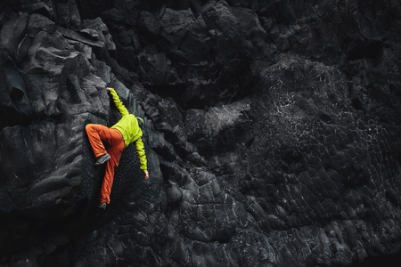 male rock climber. rock climber climbs on a black rocky wall on the ocean bank in Iceland, Kirkjufjara beach. man makes hard move without rope.の写真素材