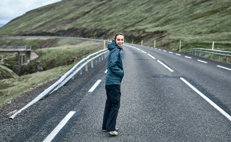 Young laughing girl outstretching hand asking to follow her on background of mountain road, Iceland,...