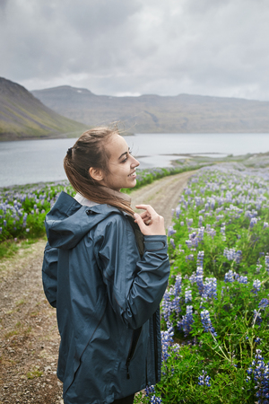 Beautiful Icelandic landscape with woman in a field of lupins in the foreground and the mountains and the fjords and the ocean in the backgroundの写真素材
