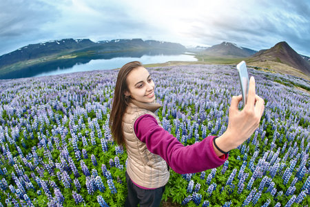 Girl in warm clothing standing in field of flowers on background of mountains and sea of Iceland and...