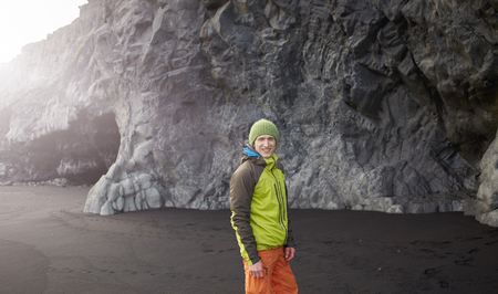 man traveler in colorfull waterproof clothes walking on Kirkjufjara black sand beach, southern Iceland.の写真素材