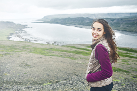 Girl in warm clothing observing surroundings on background of mountains and sea of Iceland.の写真素材