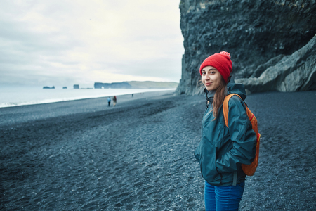 woman traveler with small orange backpack walking on black sand beach, southern Iceland.の写真素材
