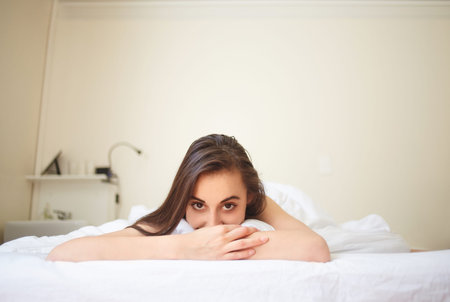 portrait of young woman lies in bed early in the morning and with a satisfied smile looks at camera