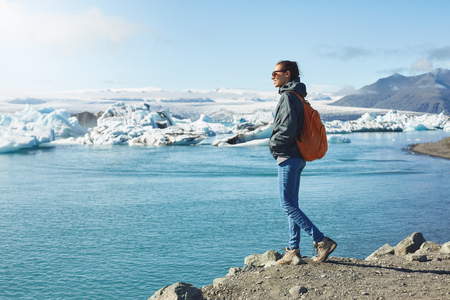 portrait of girl in warm clothing with orange backpack in Ice Lagoon in Iceland with background of sea and sky.の写真素材