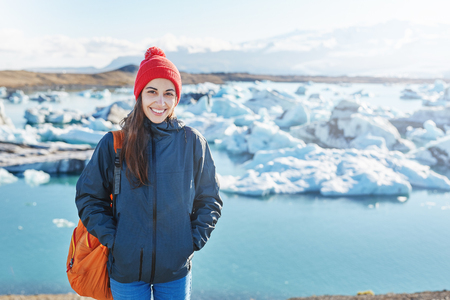 portrait of girl in warm clothing with orange backpack in Ice Lagoon in Iceland with background of sea and sky.の写真素材