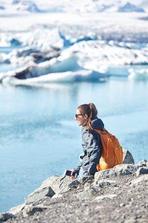 portrait of girl in warm clothing with orange backpack in Ice Lagoon in Iceland with background of sea and sky.の写真素材