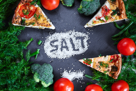 Salt, Vegetables and pieces of vegetable pie with cottage cheese, tomatoes, broccoli, dill and asparagus beans on a dark ceramic background, stone. Vegeterian food concept. The word salt is written in a layer of saltの写真素材