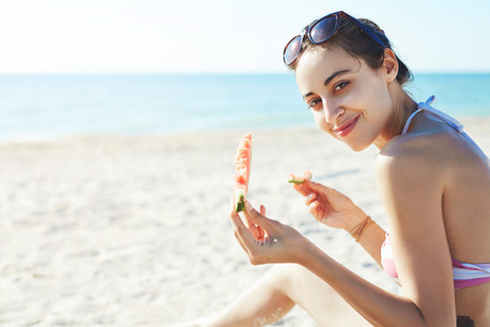 young beautiful woman eats watermelon on the beach at hot summer day, back view.の写真素材
