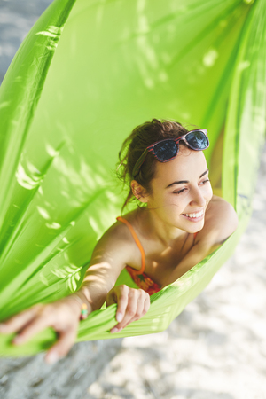 young happy woman in a bright green hammock on the beachの写真素材