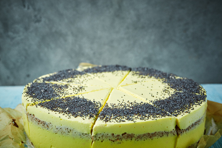 sliced mousse cake with yellow glaze and poppy seeds on the paper for baking on gray concrete wall background.の写真素材
