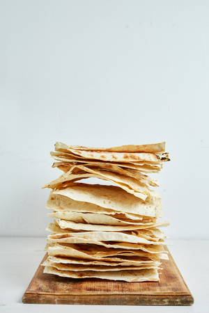 a stack of plain grilled pita bread on a wooden cutting board with a white background.の写真素材
