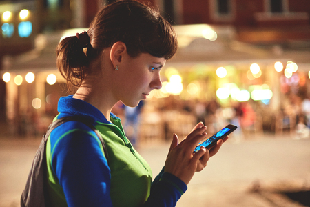 portrait of woman tourist using a smartphone at night on the street with backlightの写真素材