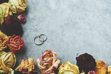 wedding rings on the dark gray concrete background in frame from dried rosesの写真素材