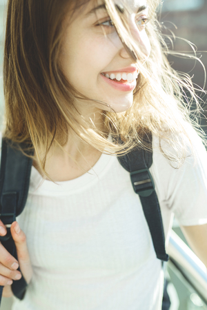 portrait of a young attcactive woman in whiti t-shirt with city backpack at sunny dayの写真素材