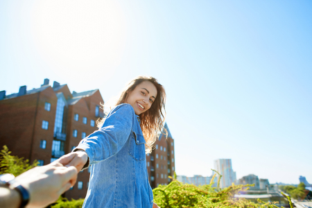 portrait of a young smiling attractive woman in jeans clothes at sunny day on the blue sky background. happy woman gives a hand to someone like follow me . first person view.の写真素材