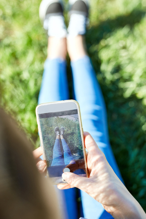 Top view of a woman sitting in a park on the grass with a phone in handsの写真素材
