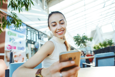 Young smiling attractive woman sitting in coffee shop in the mall using phoneの写真素材
