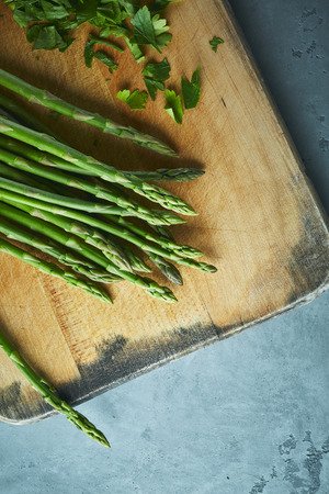 Fresh green asparagus and cutted parsley on old cutting board on gray concrete background. Top view of Food background, Ingredients for cooking.の写真素材