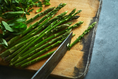 wooden cutting board with asparagus, cutted parsley and basil on gray concrete background. Cooking food.の写真素材