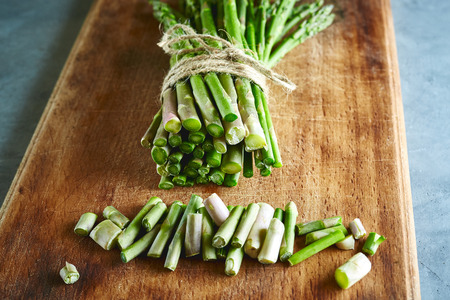 top view of bunch of fresh raw garden asparagus on rectangular wooden cutting board on gray concrete background. Ingredients for cooking. Food background.の写真素材