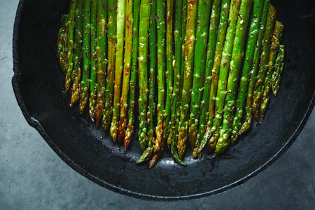 roasted asparagus with oil and spices in Cast-iron pan on the dark stone background. Vegetfrian and vegan food cooking. Top vievの写真素材