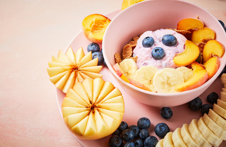 Top view of Super Healthy breakfast bowl: berry greek yoghurt with frefh blueberries, peach, banana and flakes in the pink bowl on the pink wooden table.の写真素材